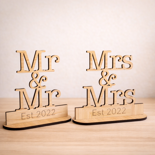 Wooden signs with 'Mr & Mr' and 'Mrs & Mrs Est 2022' on a light background