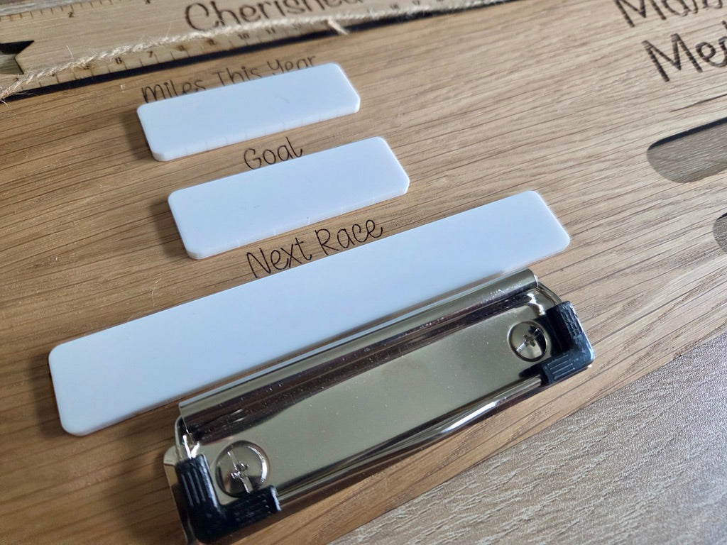 Close-up of personalised running medal display showing custom engraved name, race bib holder and dry wipe running goal tracker