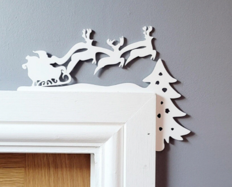 Decorative wall art with Santa's sleigh and reindeer on a white frame against a gray wall.