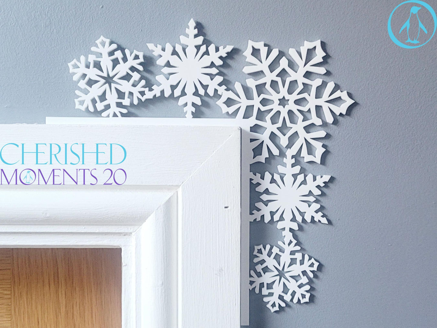 White snowflake Christmas decorations arranged in a corner on a grey wall, with a white door in the background.