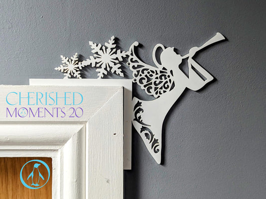 A white angel Christmas decoration sitting on a door frame, with intricate cut-out patterns in the design.