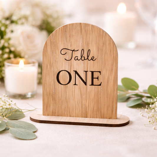 Wooden table number sign with 'Table ONE' on a decorative setting with flowers and a candle.